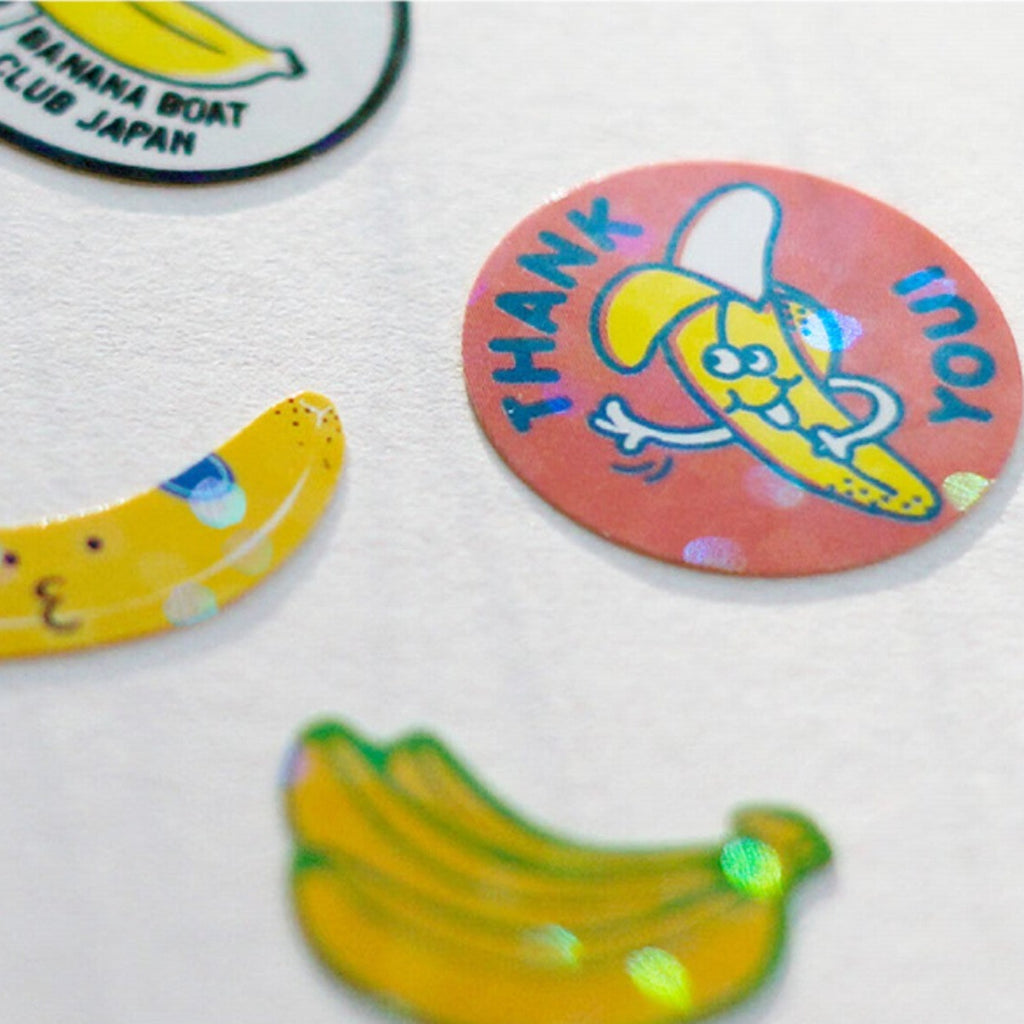Close-up of individual bakery-themed flake stickers, highlighting a playful banana design and a 'Thank You' message showcasing the holographic flakes.