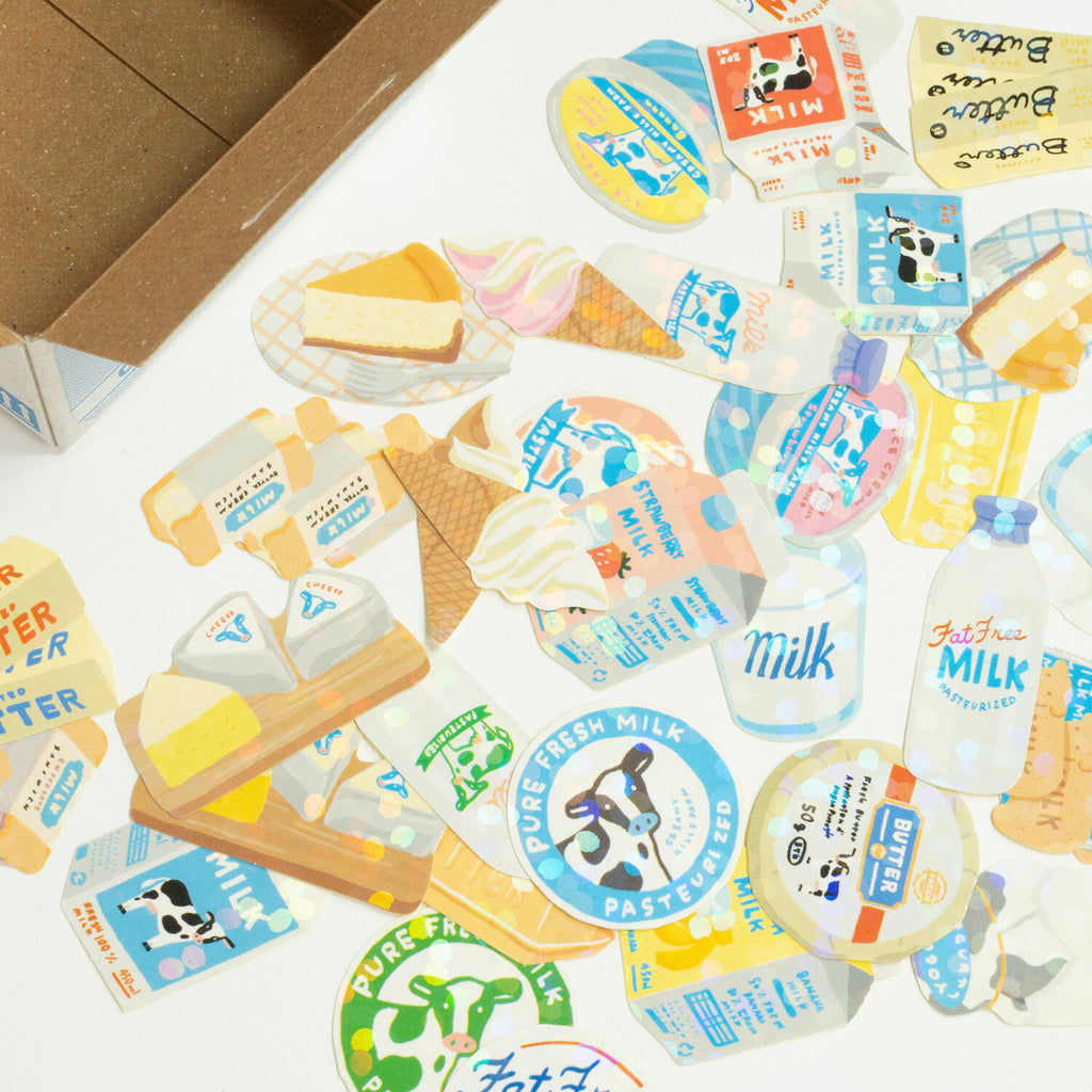 Open box of Creamy Hills Farm stickers showcasing the holographic flakes and assorted dairy designs.