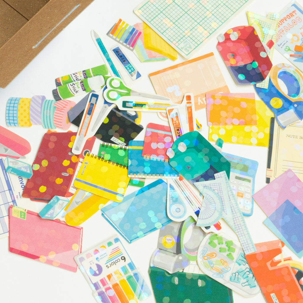 An array of scattered stationery items, including notebooks, pens, rulers, and adhesive tapes, in various patterns and colours.