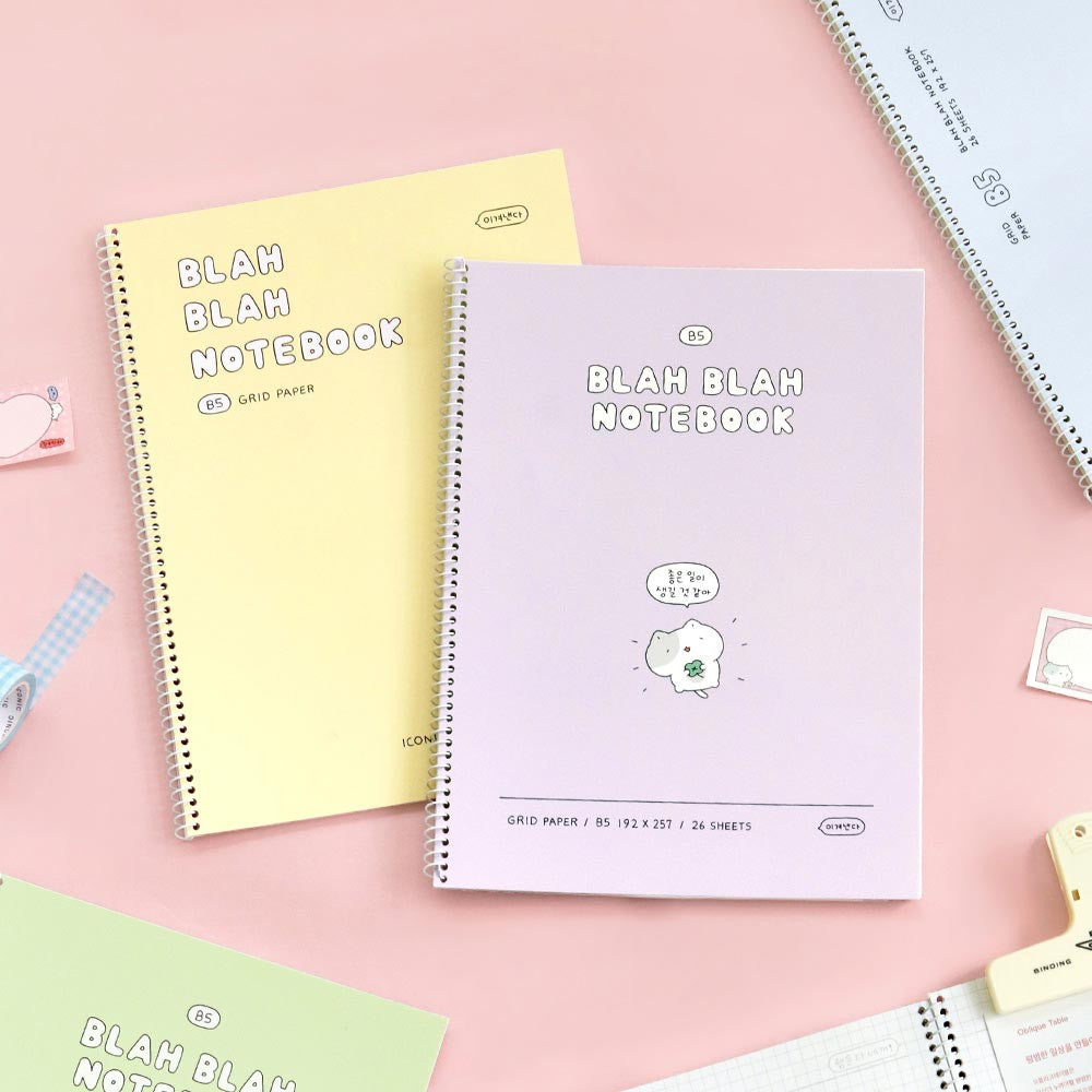 The Journal Shop - Iconic Blah Blah B5 Spiral Grid Notebooks in cream yellow and lavender displayed on pink background with stationery.