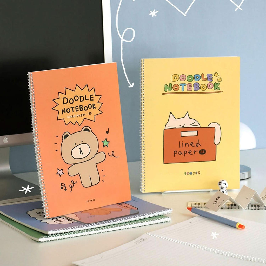 Iconic Doodle B5 Spiral Lined Notebooks in orange and yellow covers displayed on desk beside stationery.