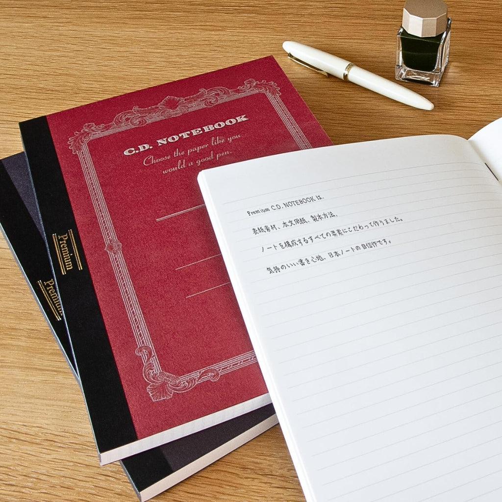 Apica Premium C.D Notebooks A4 Ruled on a wooden desk with an open notebook and writing tools.