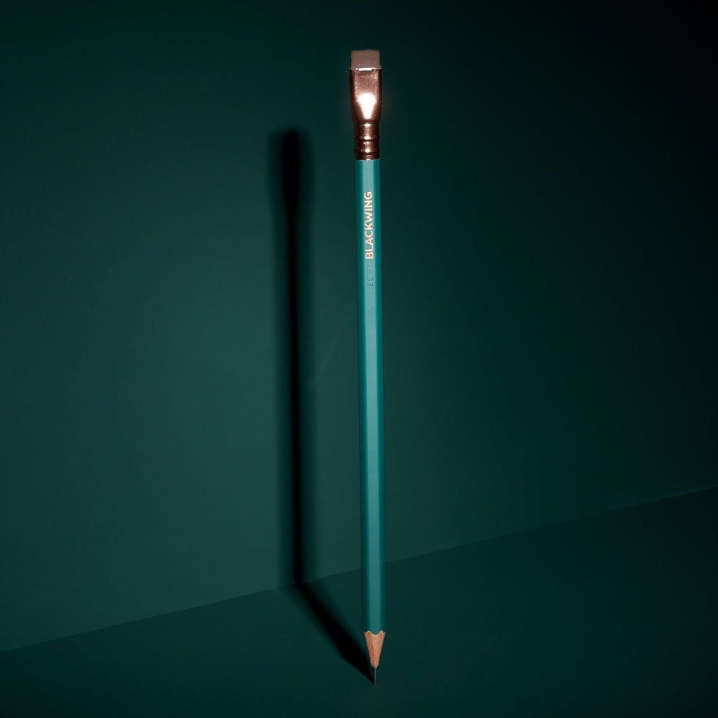 Blackwing Matte Green pencil standing upright on a dark surface with dramatic lighting.