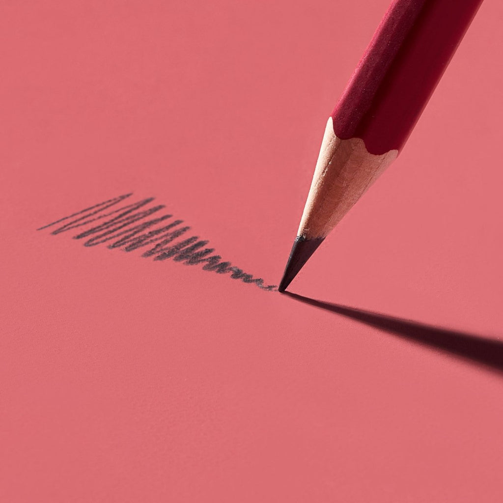 Blackwing Matte Red pencil drawing a graphite line on a textured red background.
