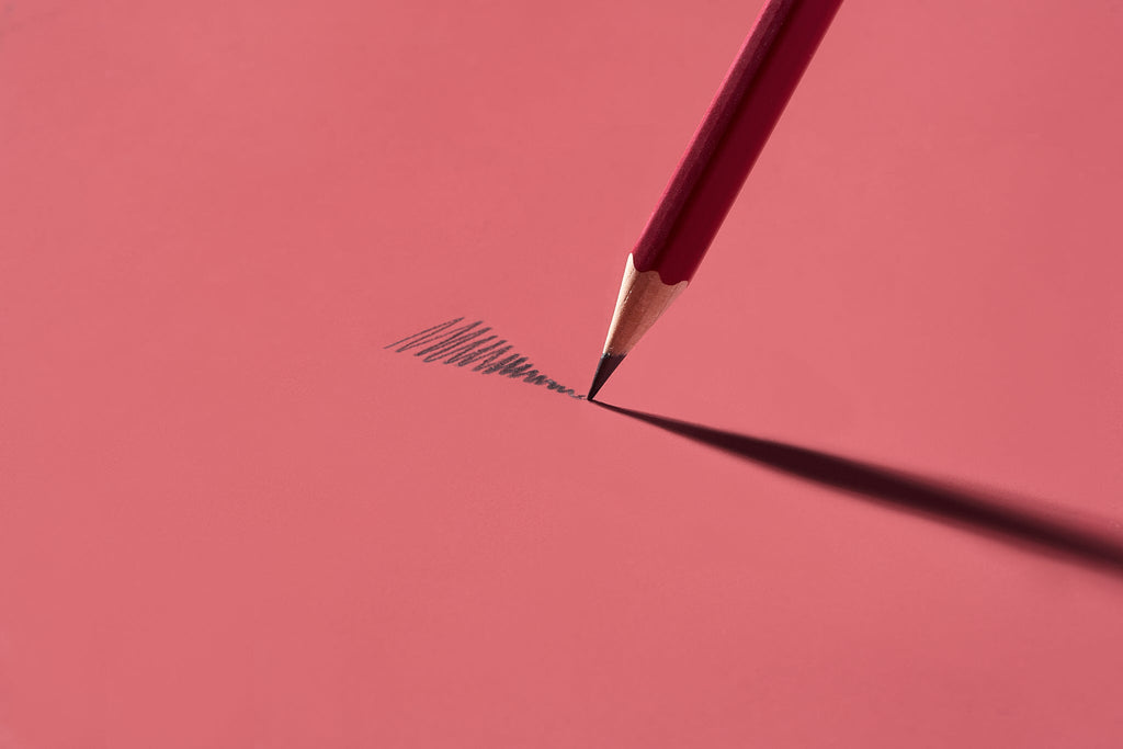 Angled Blackwing Matte Red pencil casting a long shadow on a pink-toned surface.