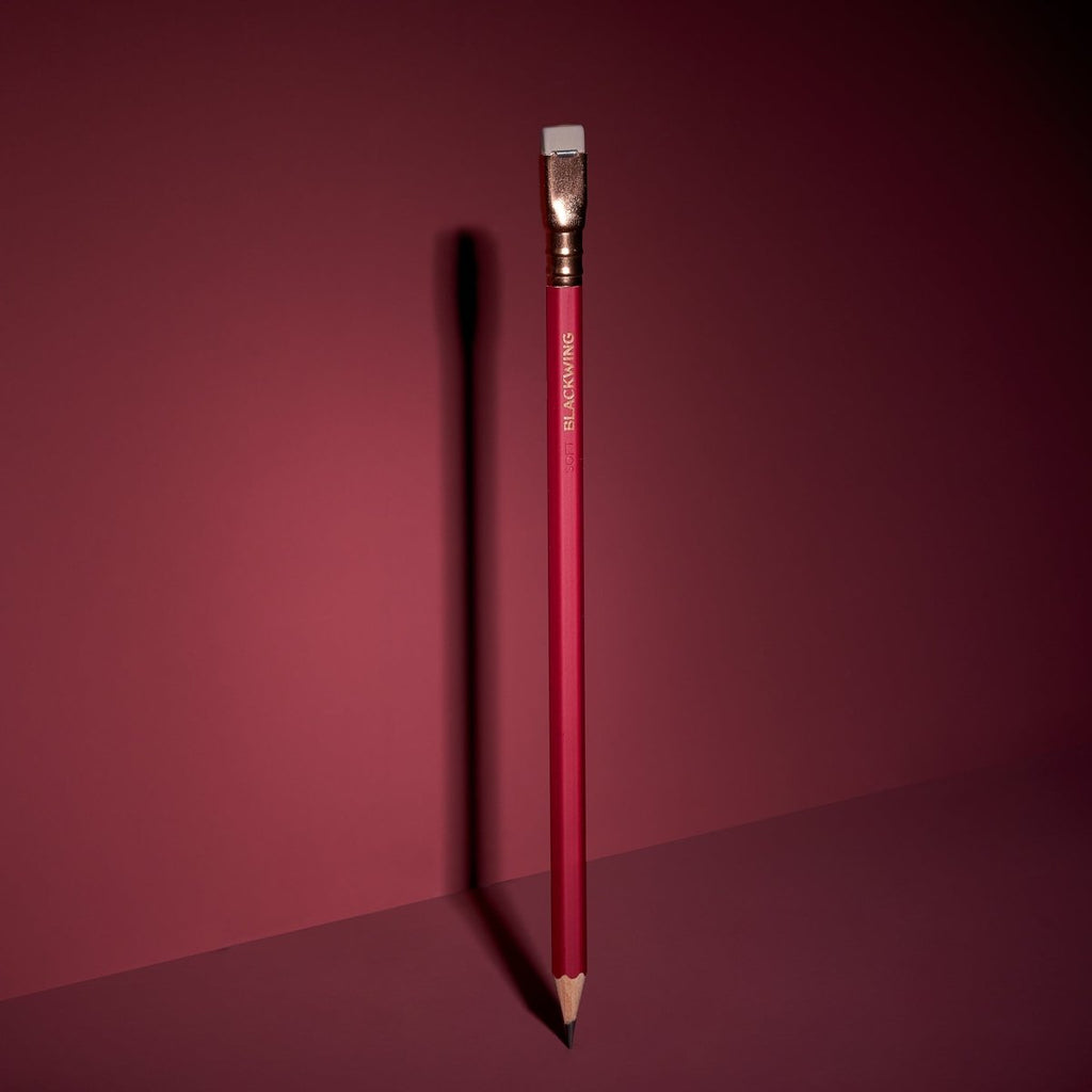 Blackwing Matte Red pencil standing upright on a red surface with dramatic lighting.