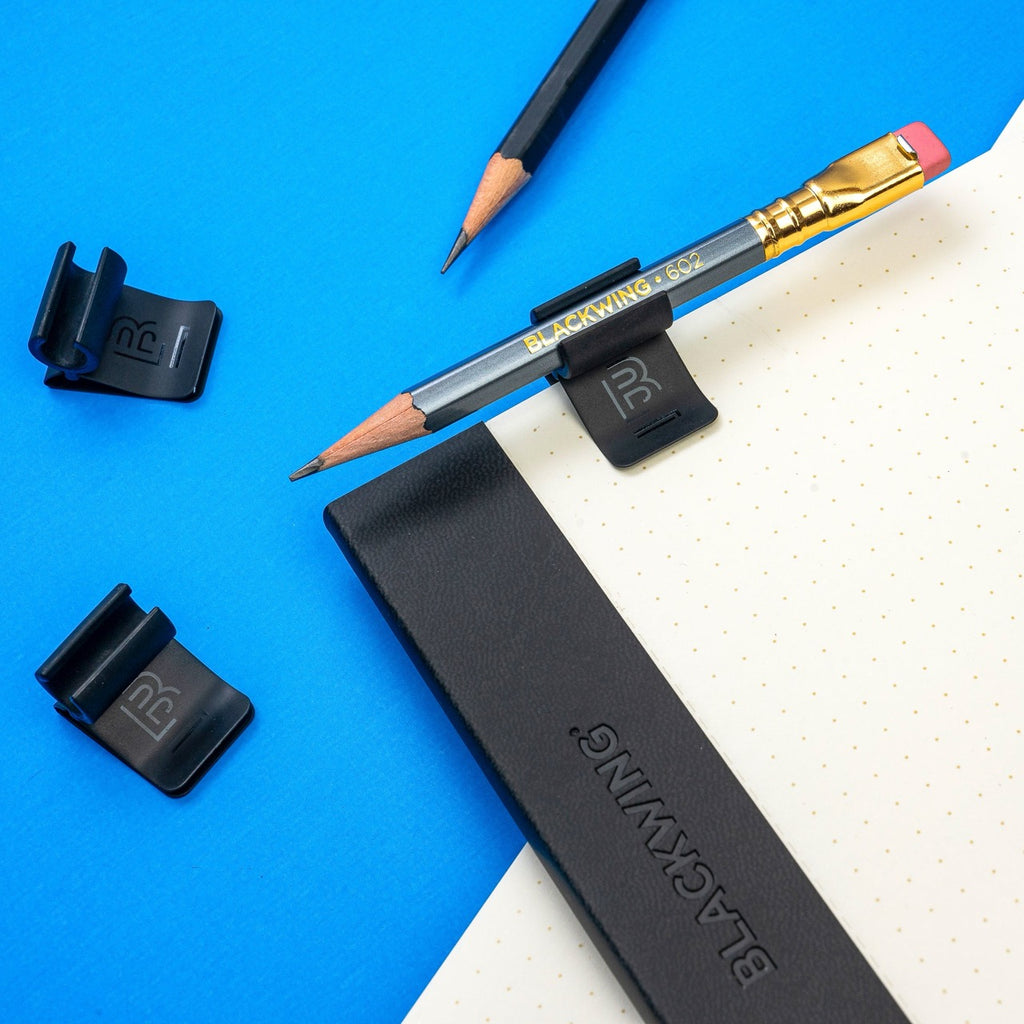 Blackwing Notebook Clip securing pencil on open book.