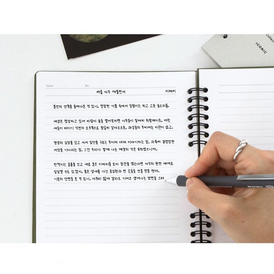 A hand writing in the Iconic Compact A5 Lined Notebook, demonstrating its practical use in a study setting.