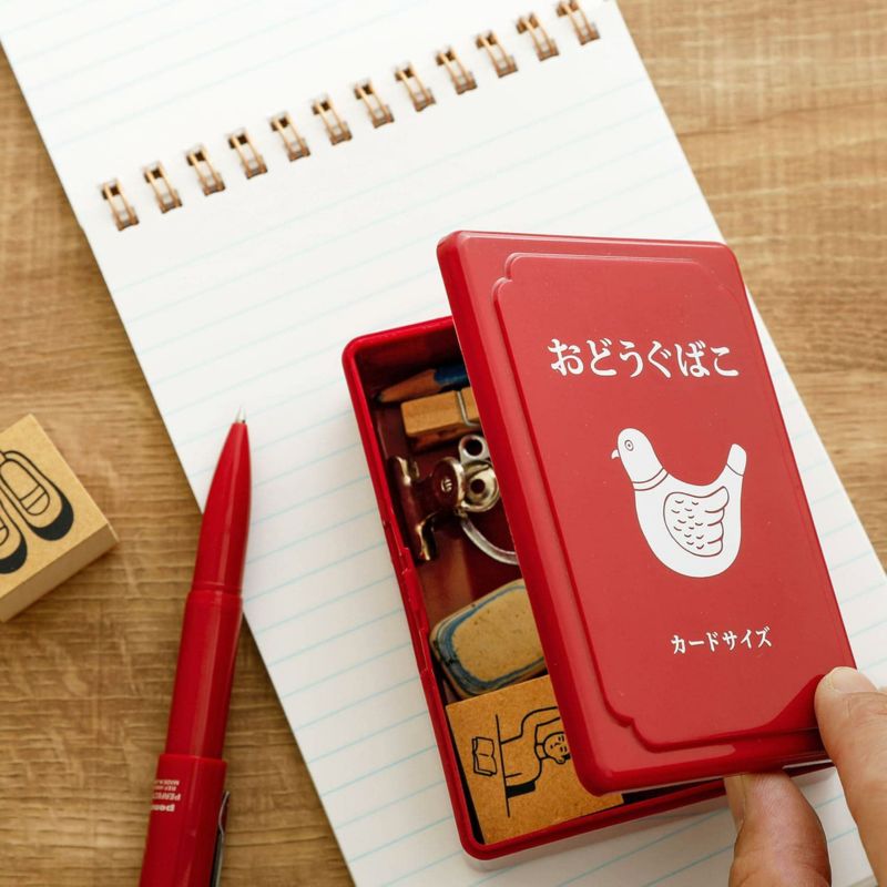 Red mini tool box open on desk with small items inside
