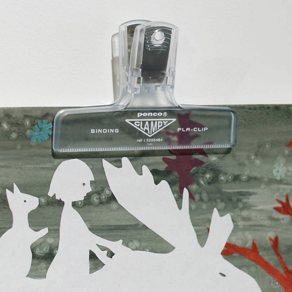 The Journal Shop - Clear Hightide Penco Clampy Pla-Clip attached to a sheet of paper on a green desk surface.