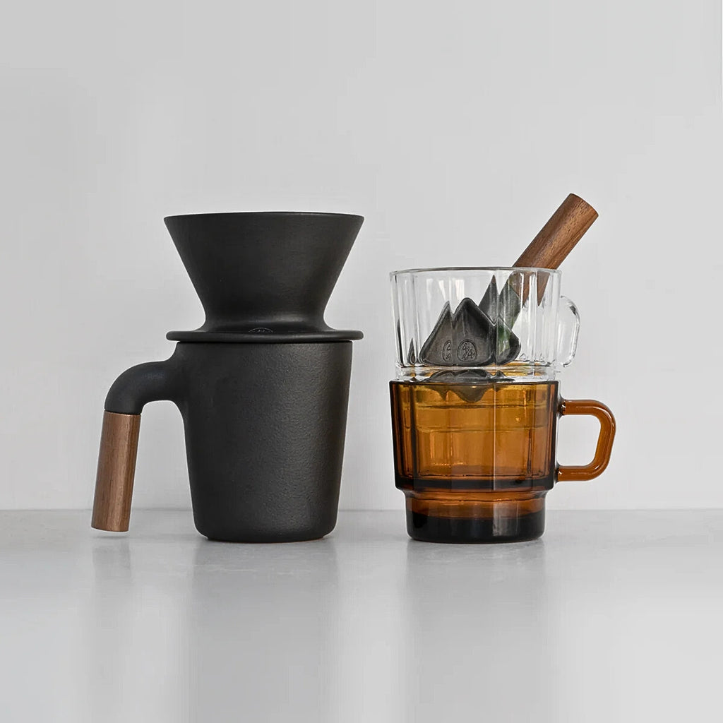 HMM Patio Coffee Dripper displayed with an amber mug and a wooden-handled coffee scoop filled with beans on a light surface.