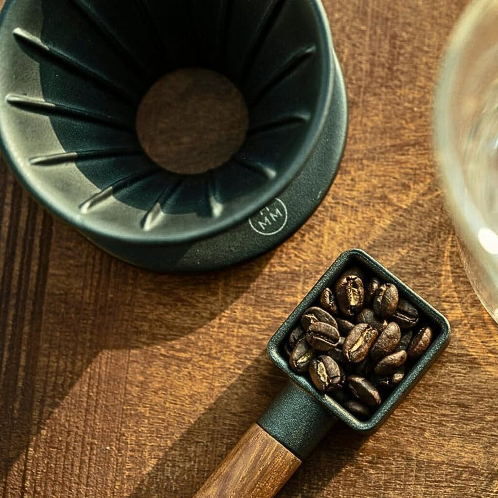 Close-up lifestyle image of the HMM Patio Coffee Dripper with a scoop of coffee beans on a wooden surface.