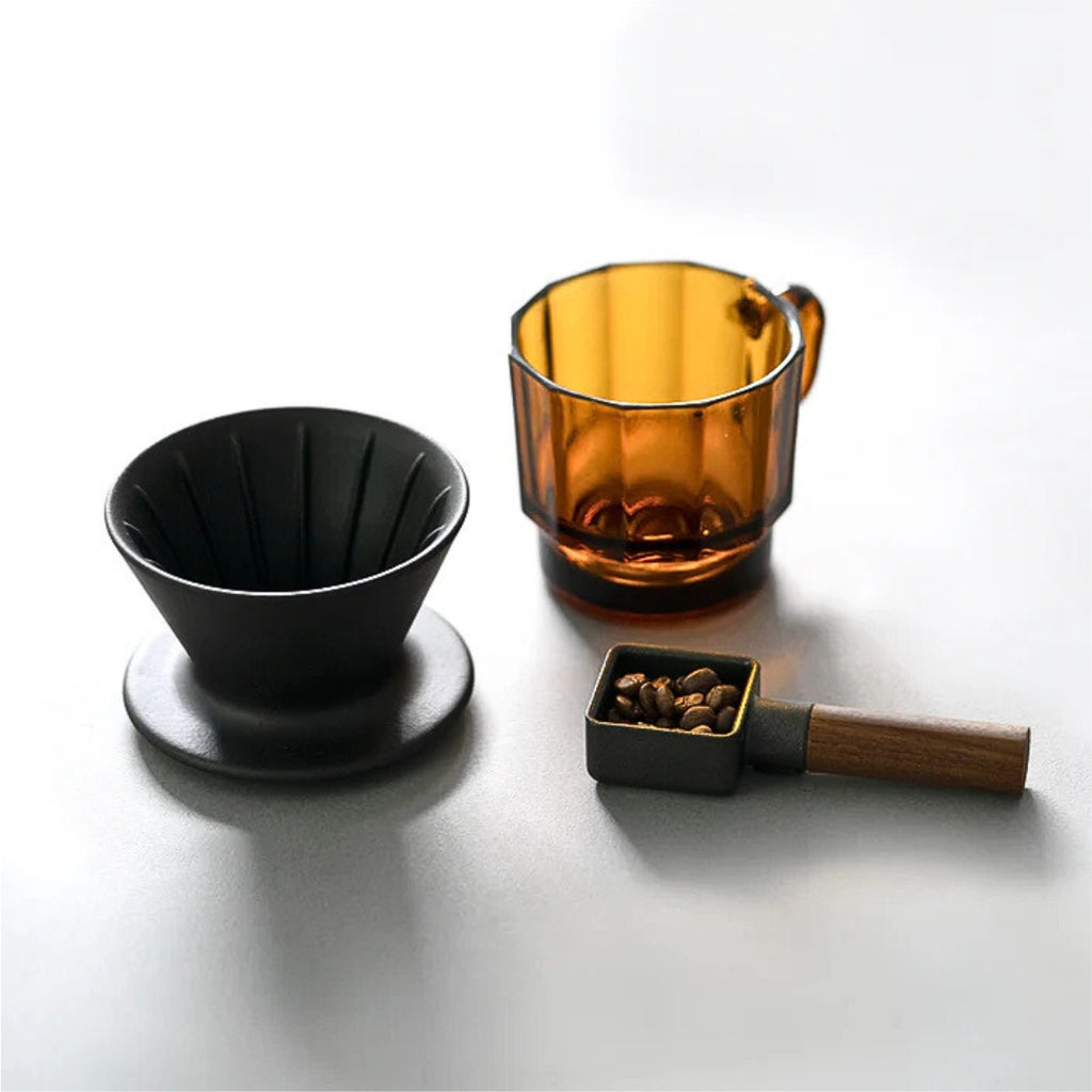 HMM Patio Coffee Dripper shown alongside an amber glass mug with brewing accessories arranged on a clean, minimalist surface.