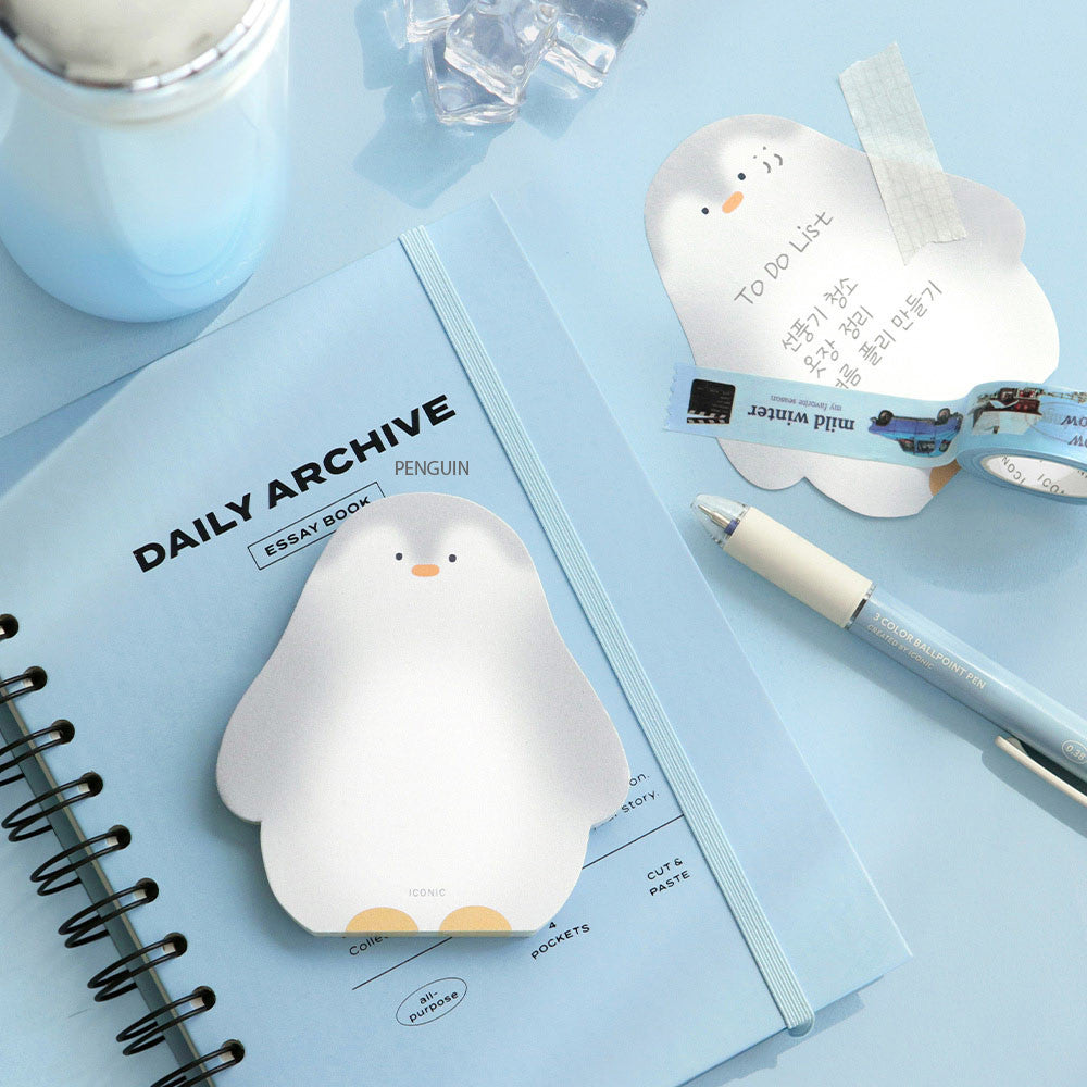 The Journal Shop - A penguin-shaped Iconic Animal Memo Pad opened on a light blue desk with stationery and a close notebook.