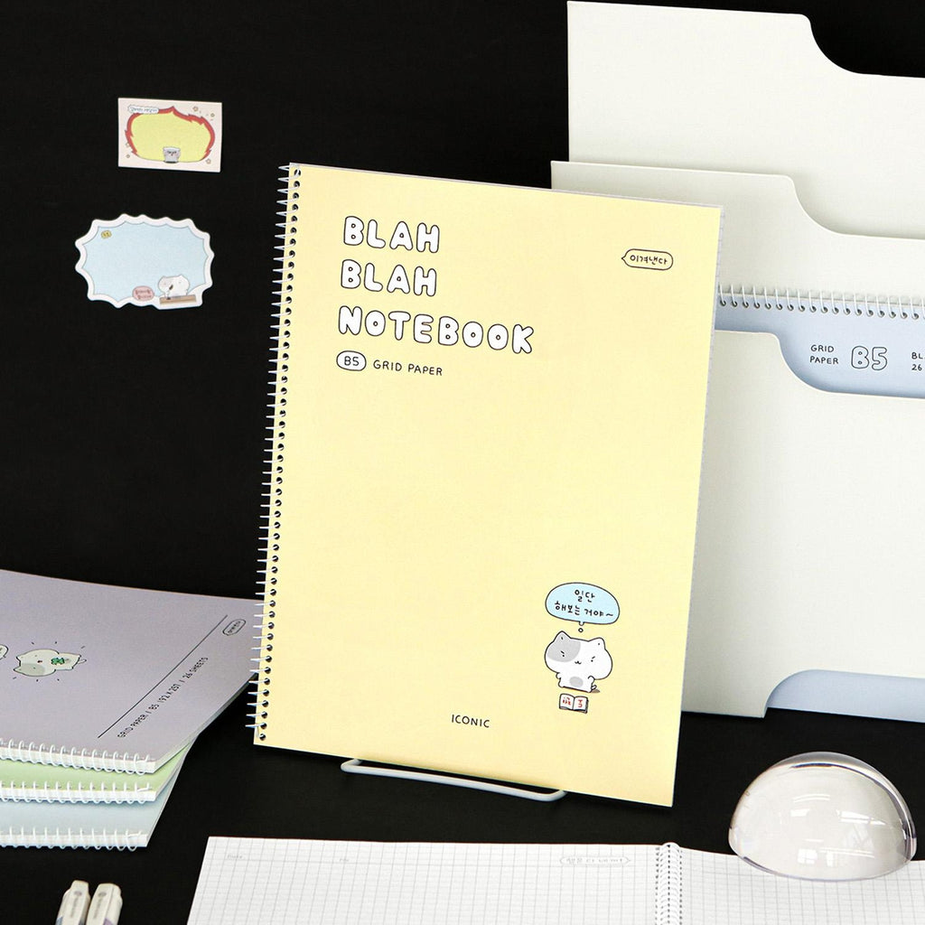 The Journal Shop - Iconic Blah Blah B5 Spiral Grid Notebook cream yellow cover displayed with black background and decorative items.