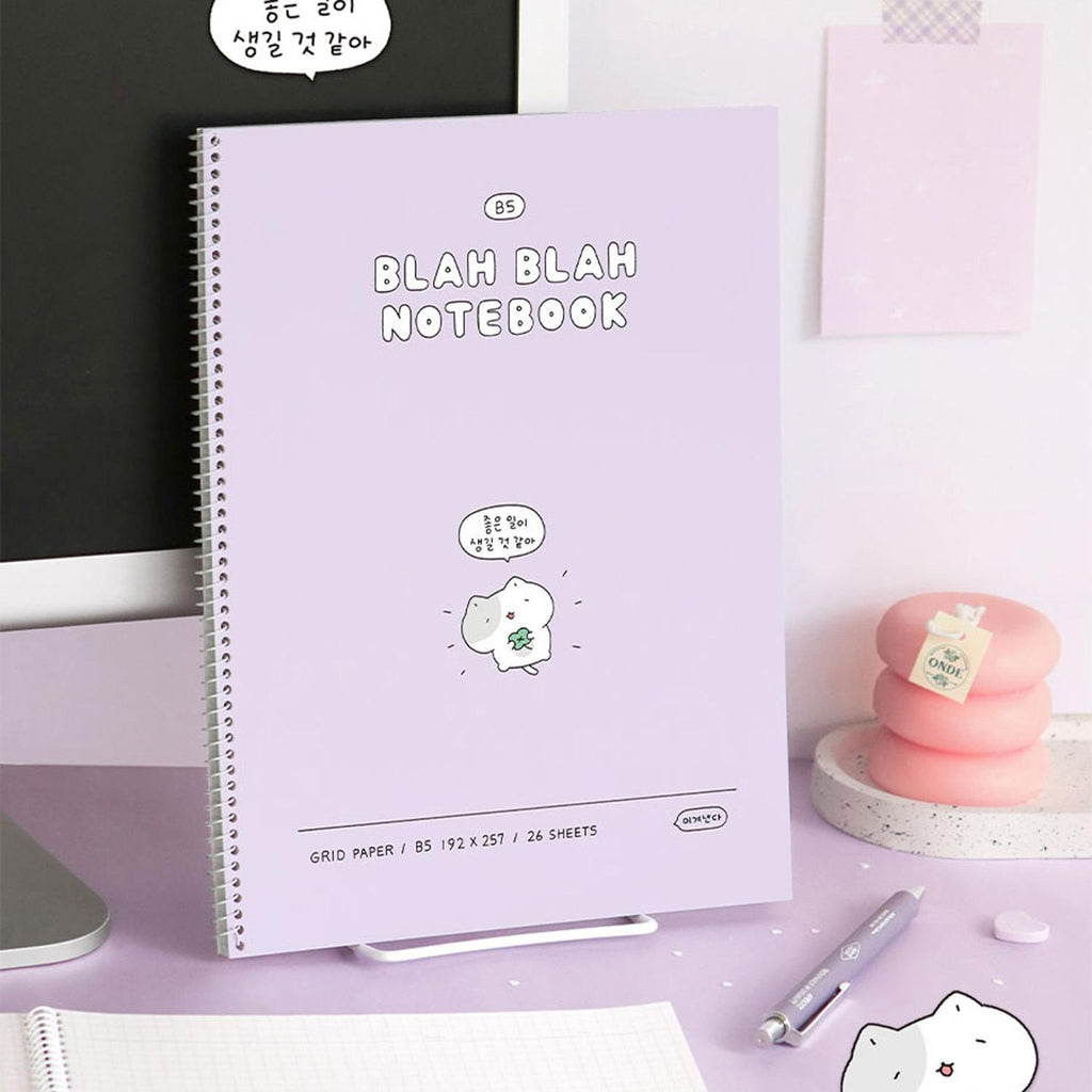 The Journal Shop - Iconic Blah Blah B5 Spiral Grid Notebook lavender cover shown with pink candle and desk setup.