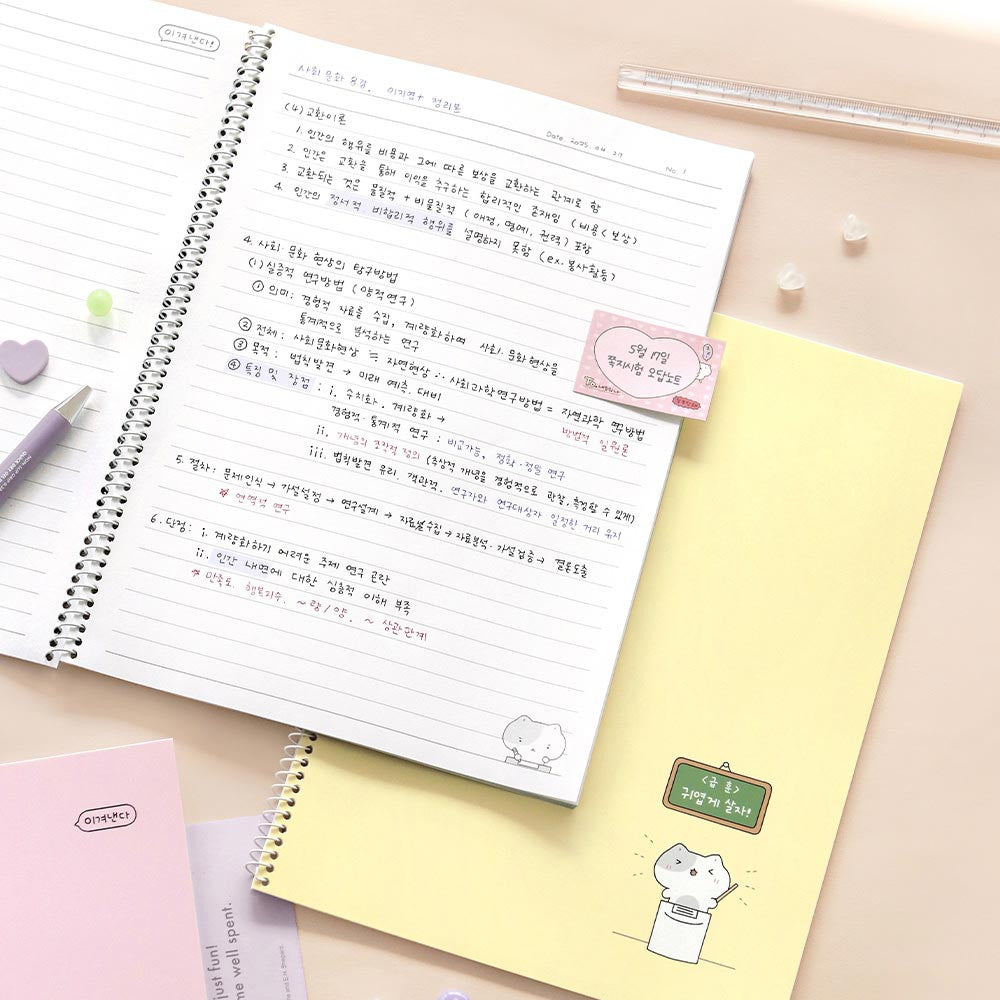 The Journal Shop - Iconic Blah Blah B5 Spiral Lined Notebook open on desk with writing and pastel yellow notebook beneath.