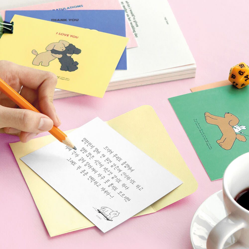 The Journal Shop - Person writing on Iconic Cuddly Message Card beside open yellow box and stationery items.