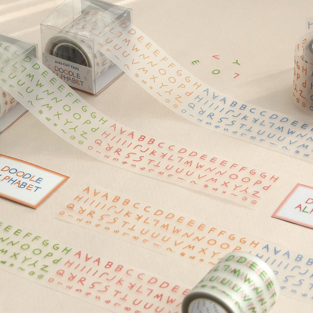 The Journal Shop - Rolls of Iconic Doodle Alphabet Kiss-Cut Tape laid out on a beige surface showing rows of pastel-coloured letters in red, green, and blue.