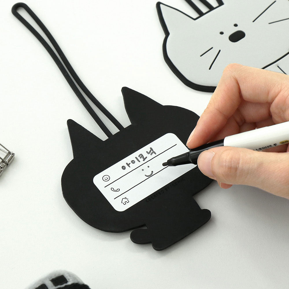 The Journal Shop - Hand writing personal information on the back of a grey cat-shaped Doodle Luggage Tag.