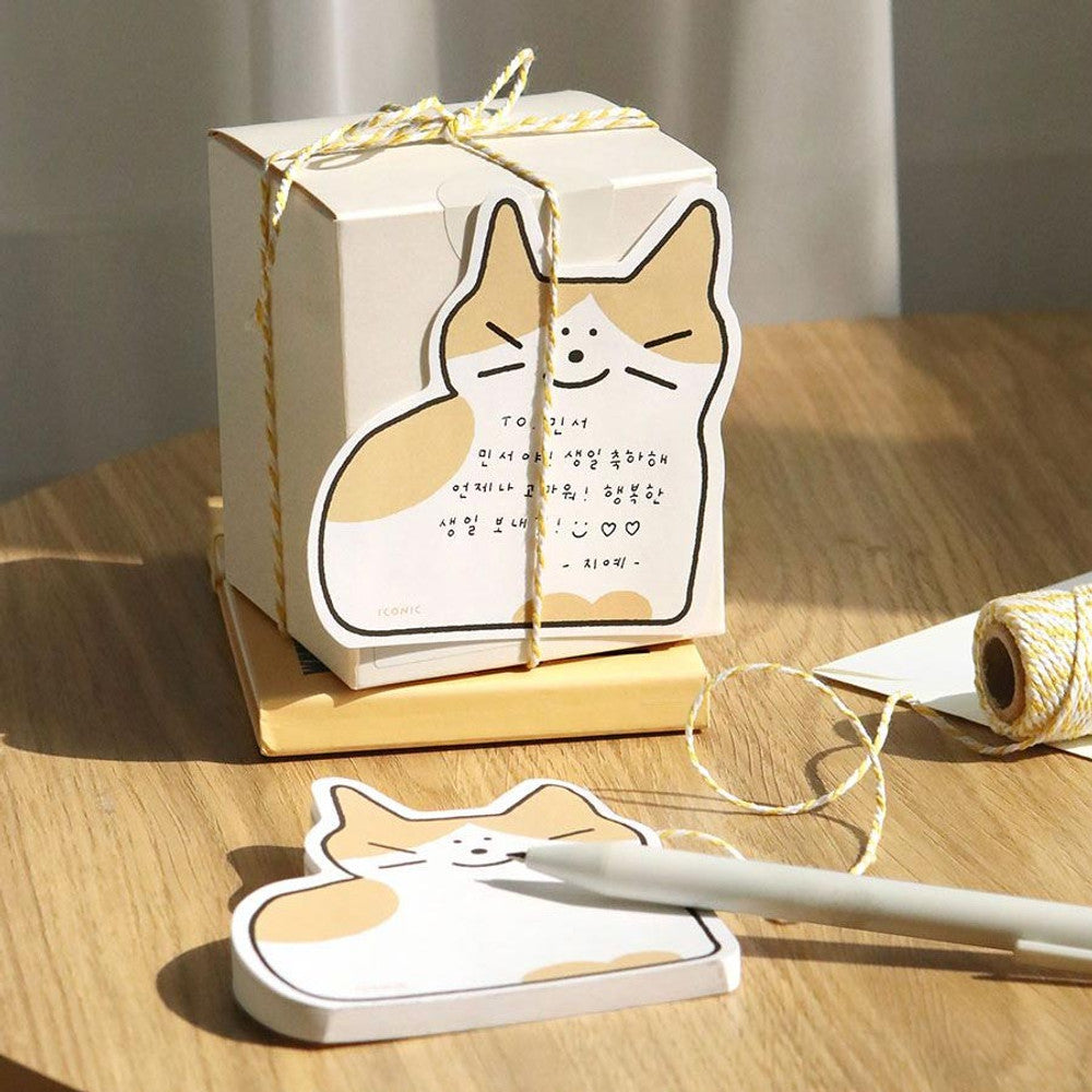 The Journal Shop - Cat-shaped Iconic Doodle Memo Pad “Cheese” used as a tear-off note and gift tag on a wrapped box with pen and string on wooden table.