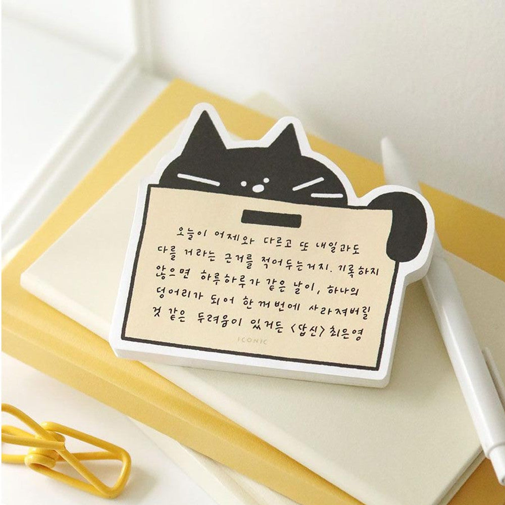 The Journal Shop - Black cat-shaped Iconic Doodle Memo Pad “Box” design with beige note space placed on stacked notebooks with pen and paperclip.