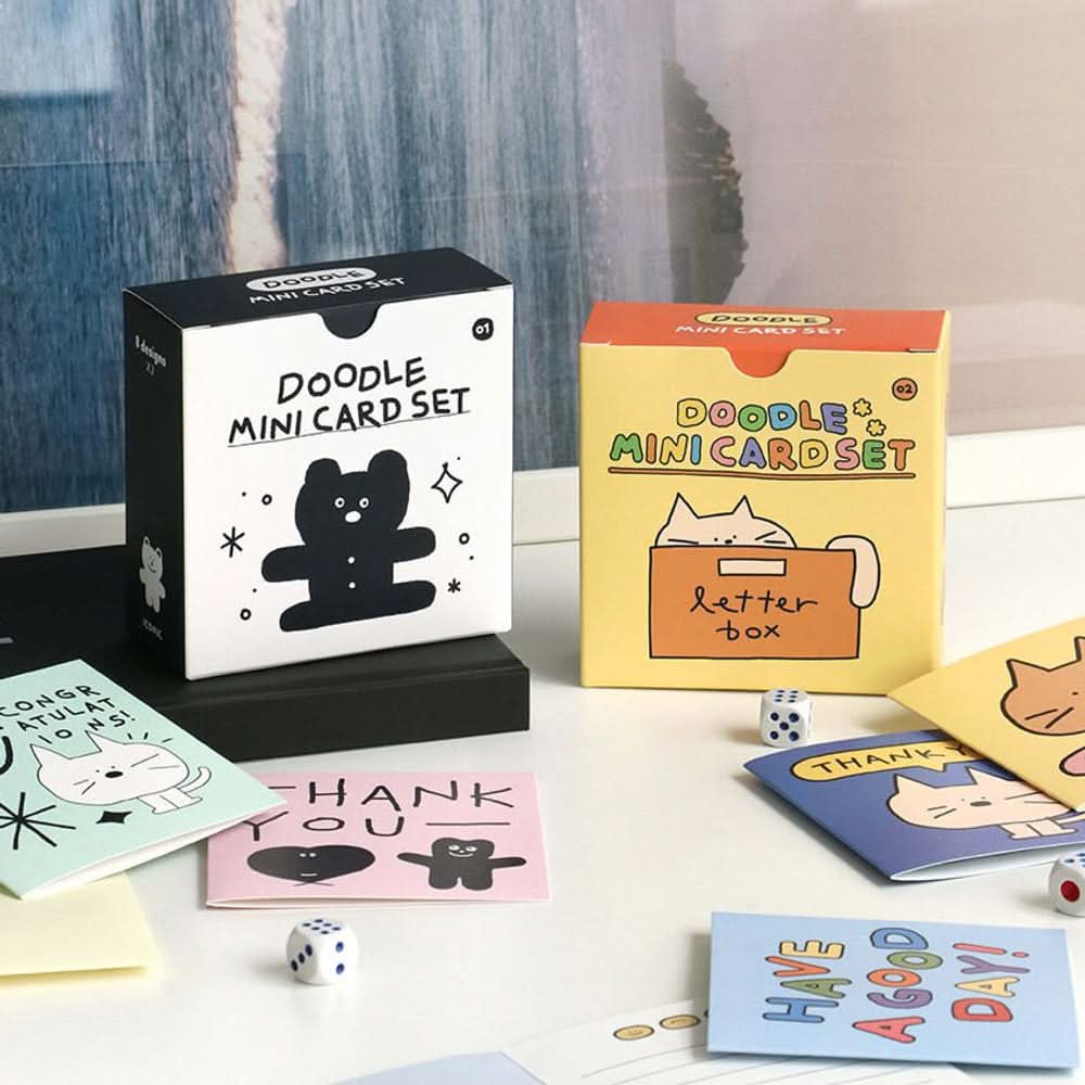 The Journal Shop - Iconic Doodle Mini Card Sets in black and yellow boxes displayed with assorted cute illustrated cards on desk.