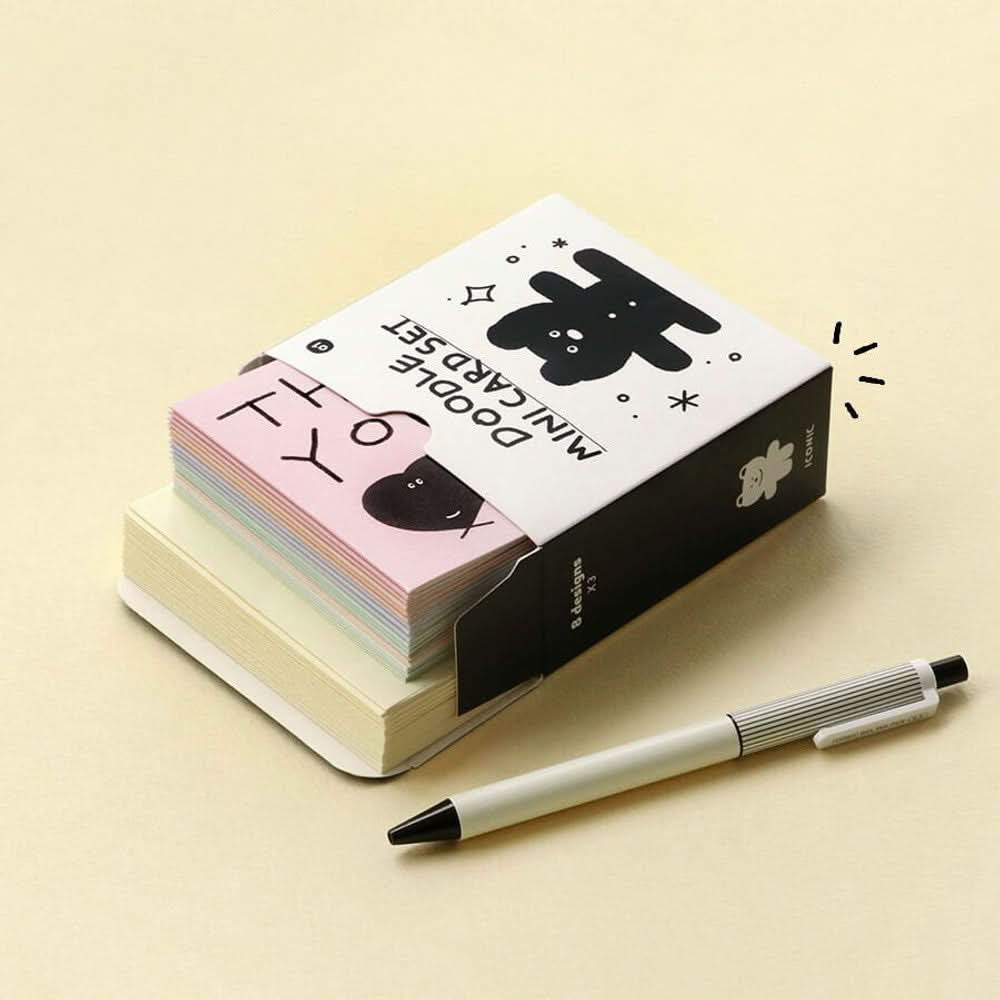 The Journal Shop - Stack of Iconic Doodle Mini Card Sets in black and yellow boxes placed beside pen and cards.