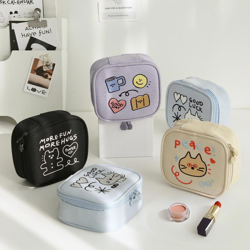The Journal Shop - Collection of Iconic Doodle Mini Pouches in cream, lavender, blue, and black displayed on a desk with makeup.