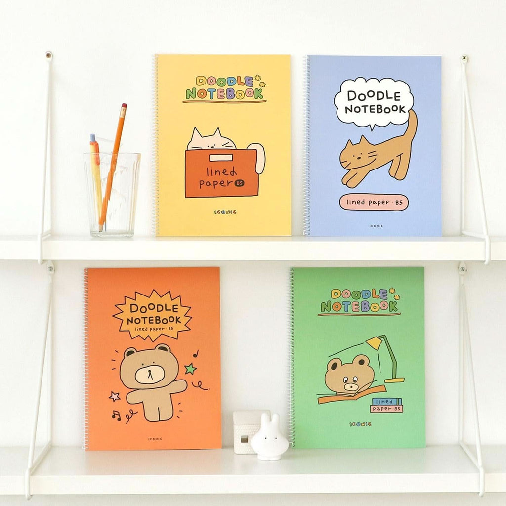The Journal Shop - Iconic Doodle B5 Spiral Lined Notebooks in orange, green, blue, and yellow with playful illustrated covers displayed on white shelf.
