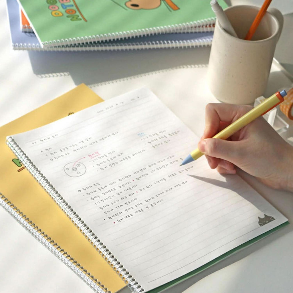 The Journal Shop - Iconic Doodle B5 Spiral Lined Notebook open while writing, showing ruled pages and neat handwriting.