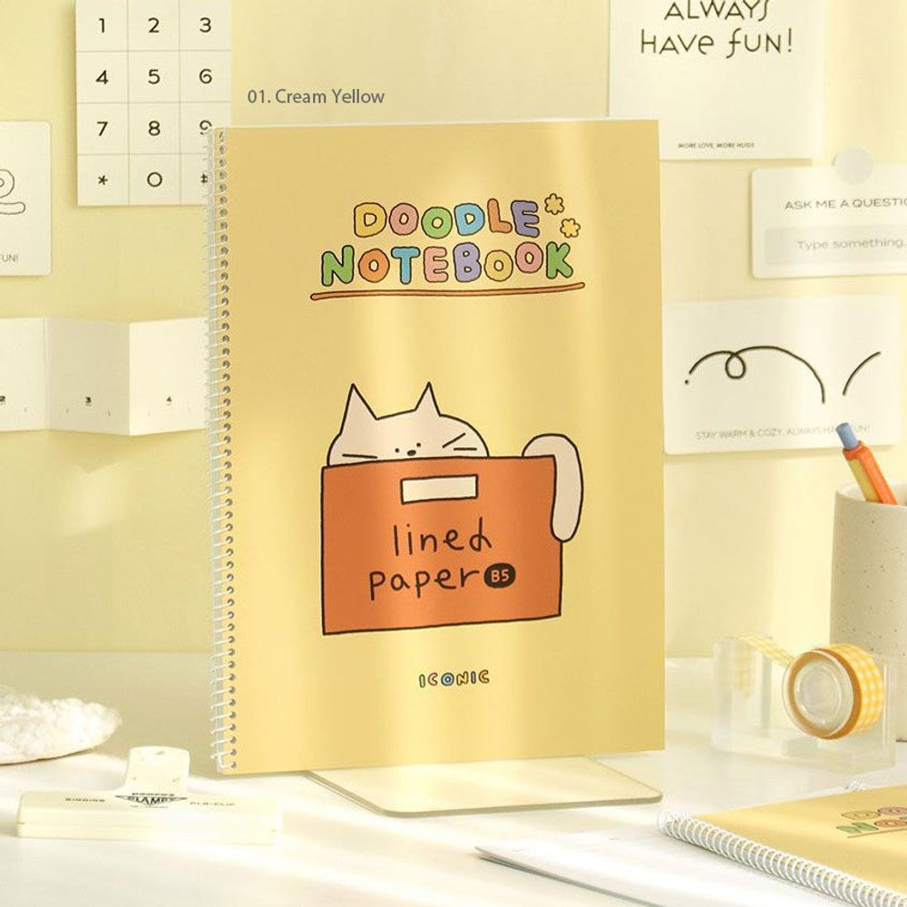 The Journal Shop - Iconic Doodle B5 Spiral Lined Notebook in yellow cover shown open with doodle cover design visible beside it.