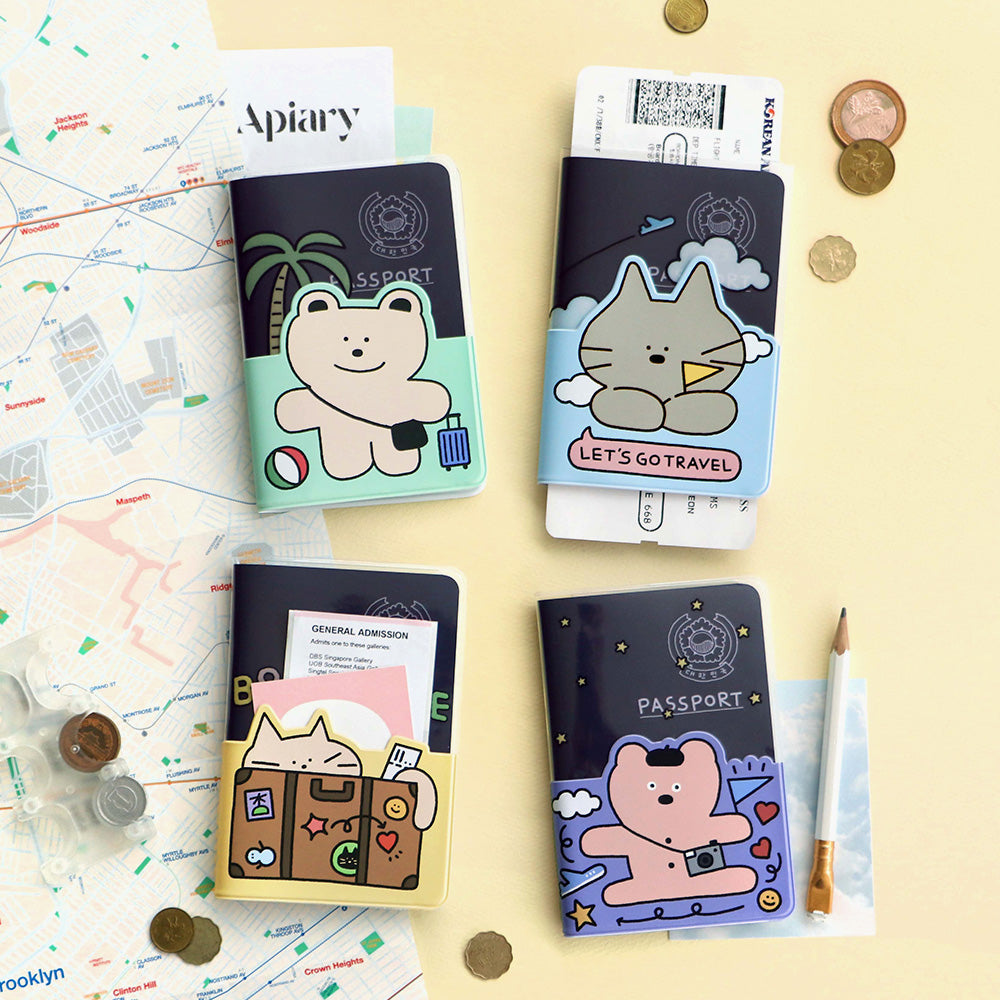 The Journal Shop - Collection of Iconic Doodle Passport Cases in assorted designs featuring playful character illustrations, displayed with travel essentials and coins.