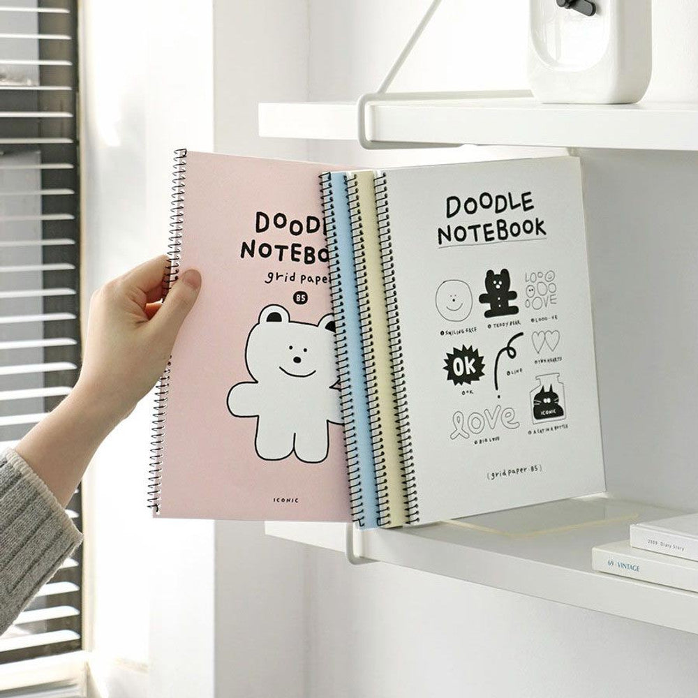 The Journal Shop - Iconic Doodle Spiral B5 Grid Notebook with pink bear cover being placed on white shelf.
