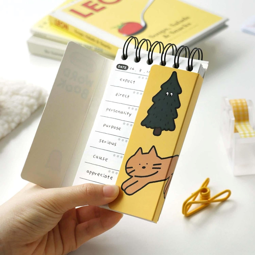 The Journal Shop - A person holding a compact yellow Iconic Doodle Word Pocket Size Notebook with a cute tree and cat design on the cover.