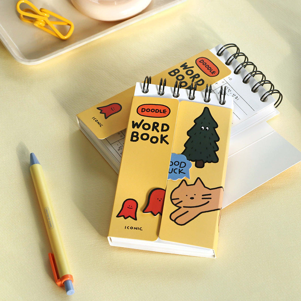 The Journal Shop - A yellow Iconic Doodle Word Pocket Size Notebook placed beside pencils and paper clips on a light desk.