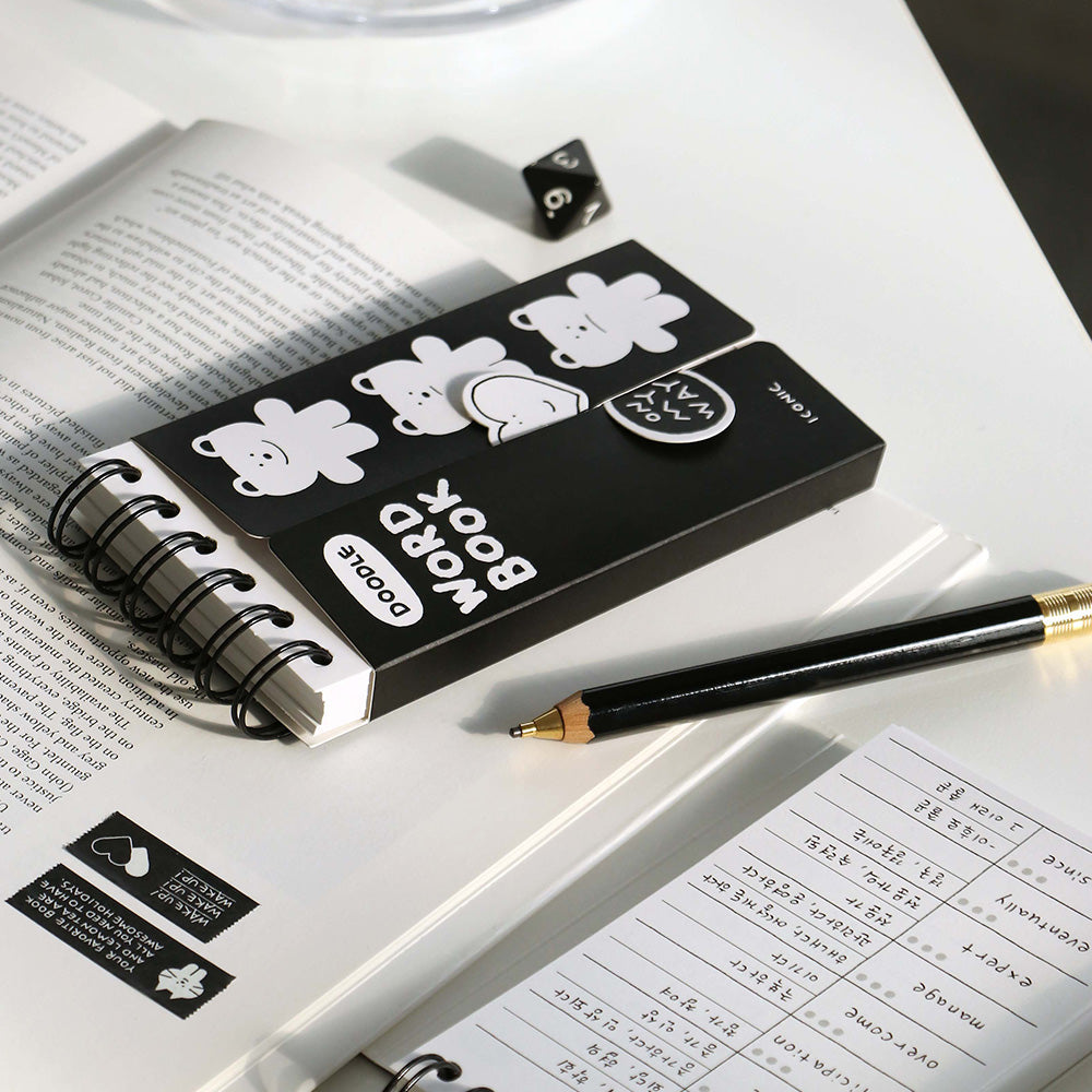 The Journal Shop - A black Iconic Doodle Word Pocket Size Notebook with cute white bear illustrations on the cover, placed on an open book with a pencil and study notes beside it on a tidy white desk.