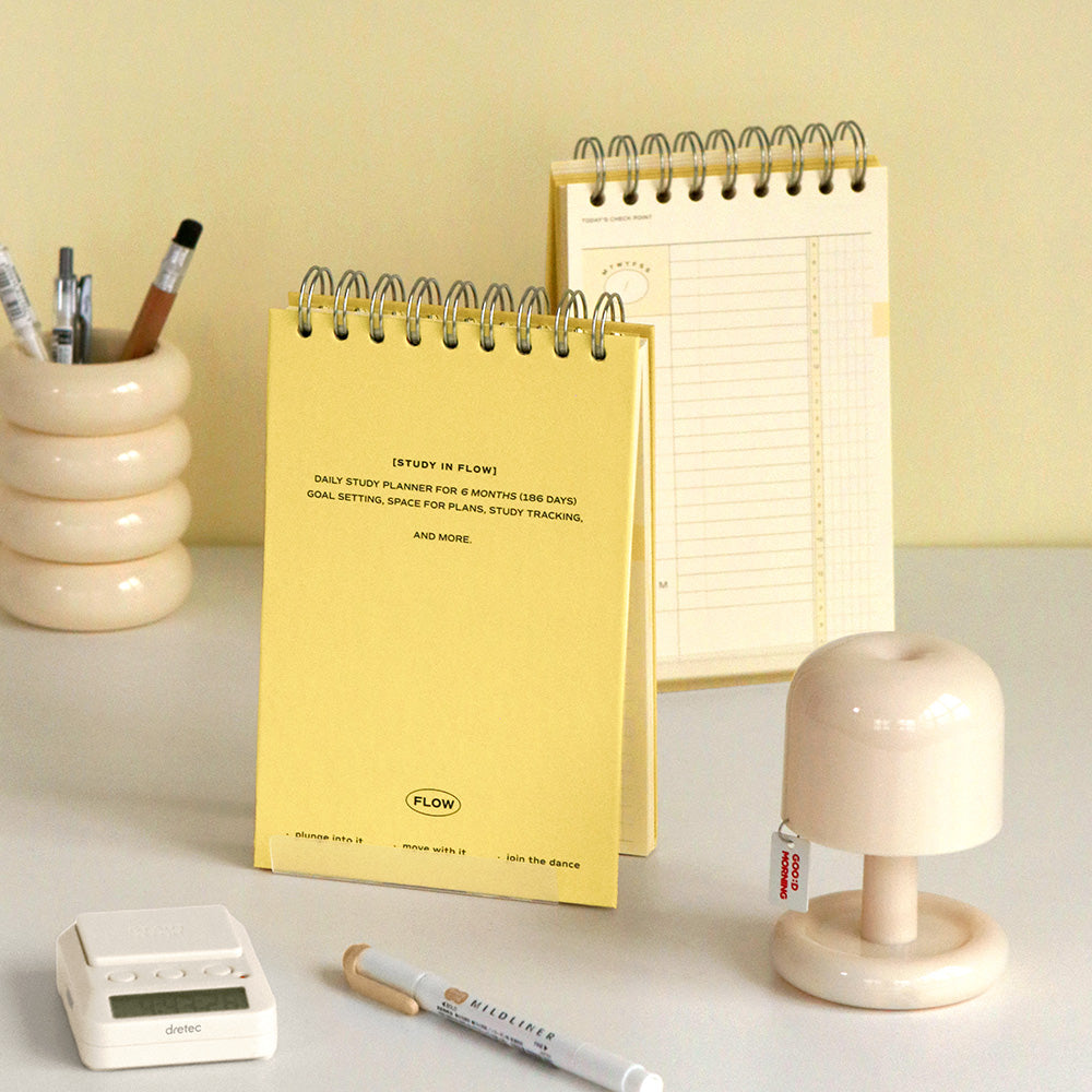 The Journal Shop - Iconic Flow B6 Spiral Study Planner in butter yellow cover displayed upright on desk with pen and stationery.