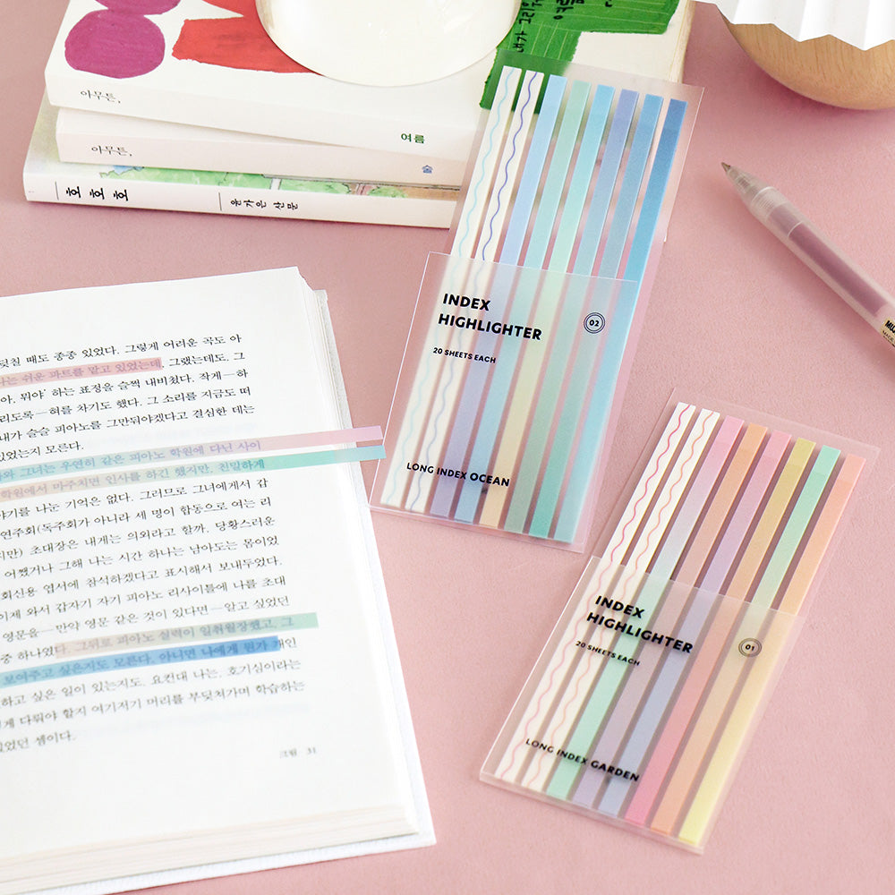 Pastel Iconic Index Long Highlighter Strips displayed on a pink desk beside an open book.
