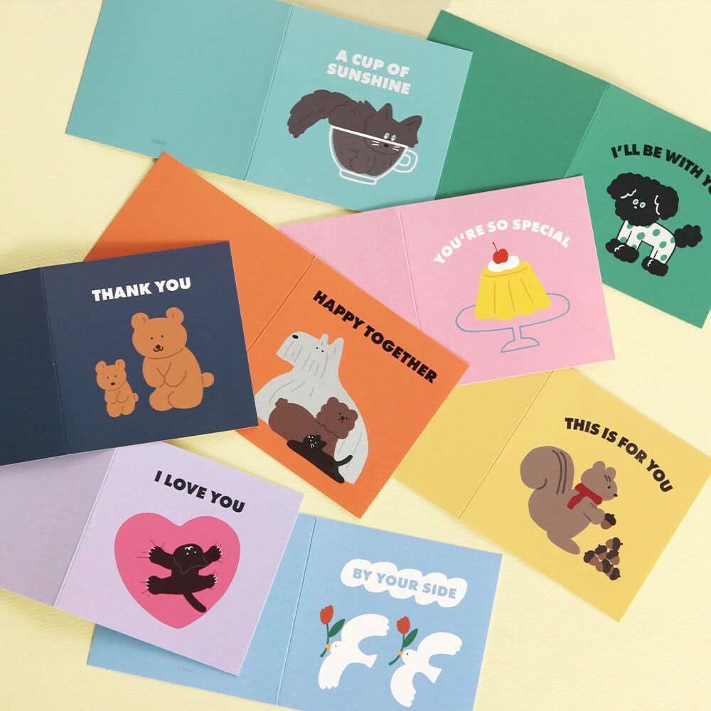 The Journal Shop - A flat lay of open Iconic Mini Friends Cards on a pastel yellow background, each featuring playful animal and dessert illustrations.