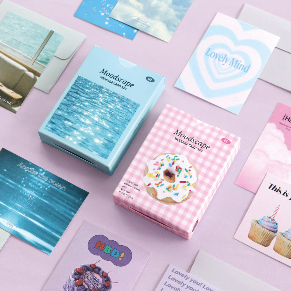 The Journal Shop - Iconic Moodscape Message Card Set in pastel blue and pink boxes with assorted cards and envelopes displayed on desk.