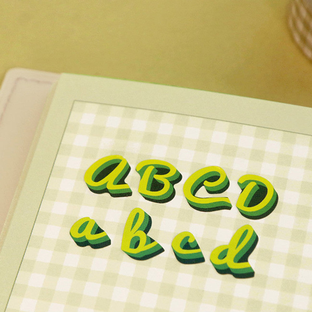 The Journal Shop - Green alphabet stickers spelling words arranged on a yellow background.