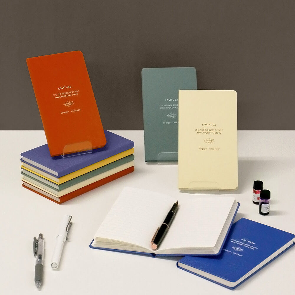 The Journal Shop - Iconic Solitude Handy Notebooks in assorted colours stacked neatly on desk with pen and ink bottle.