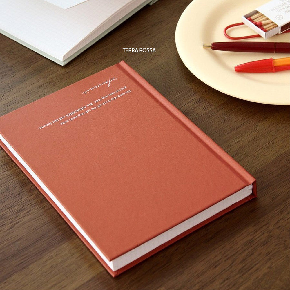 The Journal Shop - A red-orange Iconic Souvenir B6 Grid Notebook on a brown table beside stationery accessories.