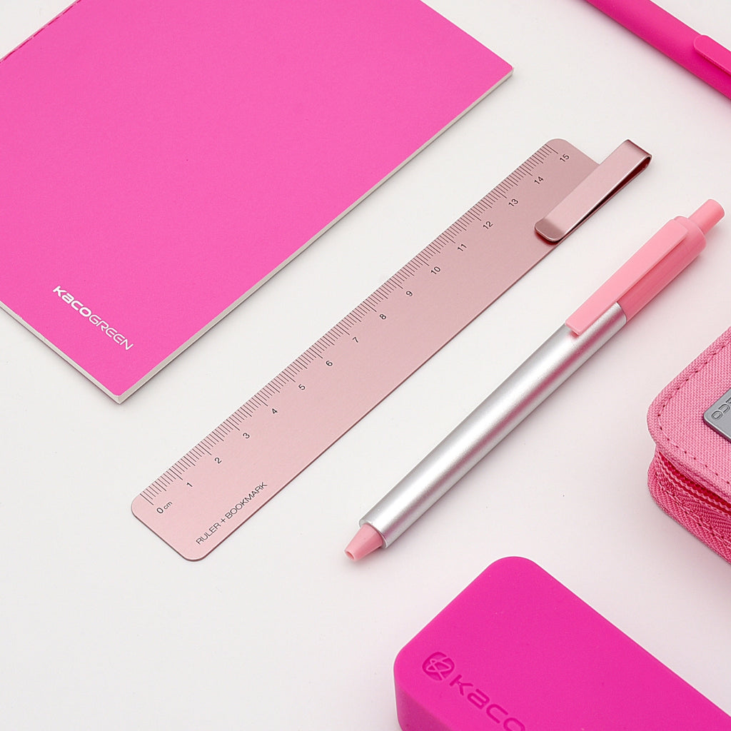 Pink metal ruler styled with matching notebook, pen, and pencil case for a coordinated desk setup.