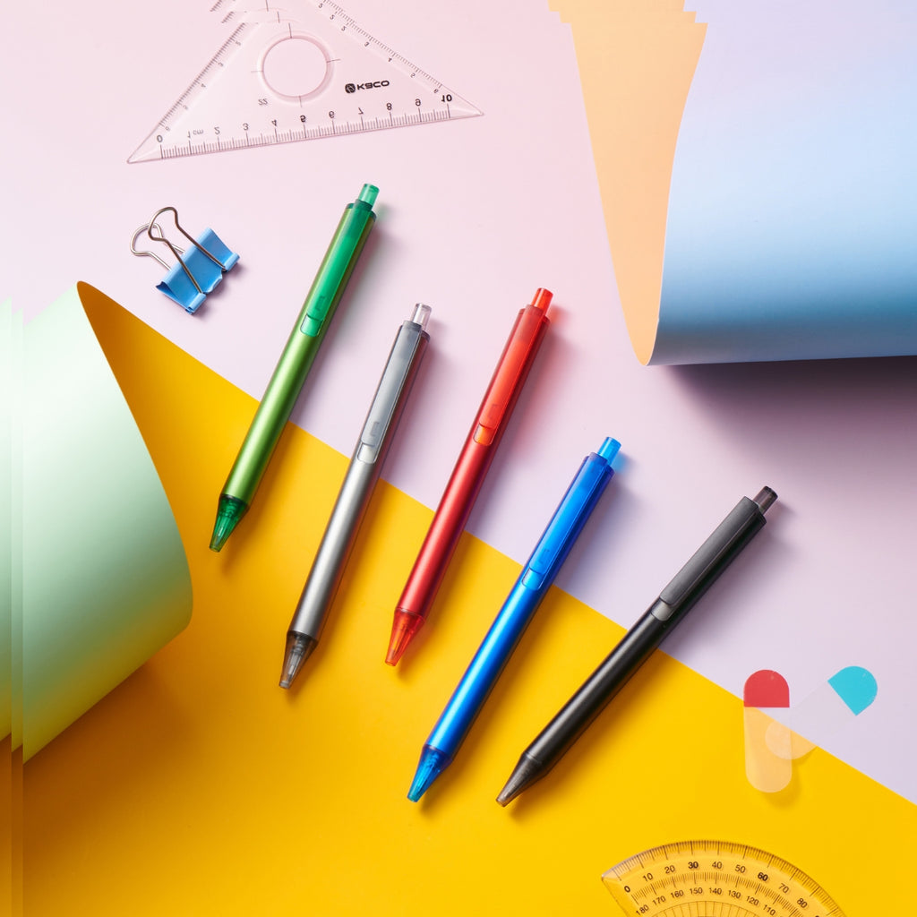 Flat lay of five Kaco Pure pens arranged diagonally on colourful pastel papers with stationery accessories.