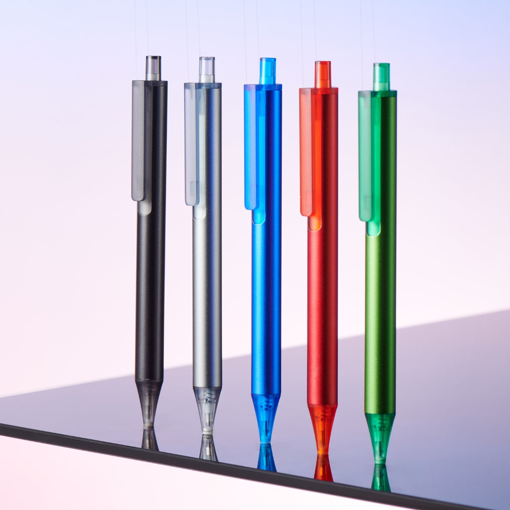 Kaco Pure pens in black, silver, blue, red, and green suspended upright against a pink gradient background.