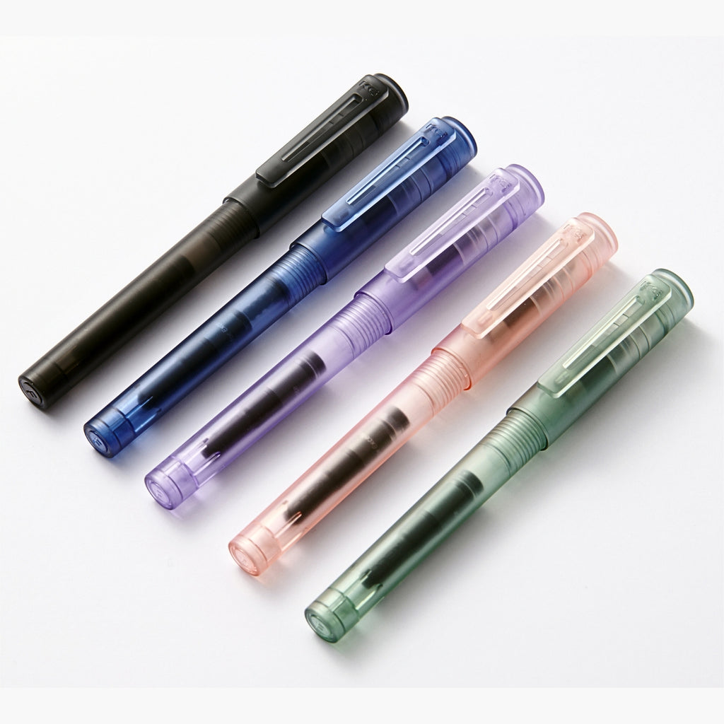 Flat lay of Kaco transparent fountain pens in black, blue, purple, pink, and green lined up side by side.