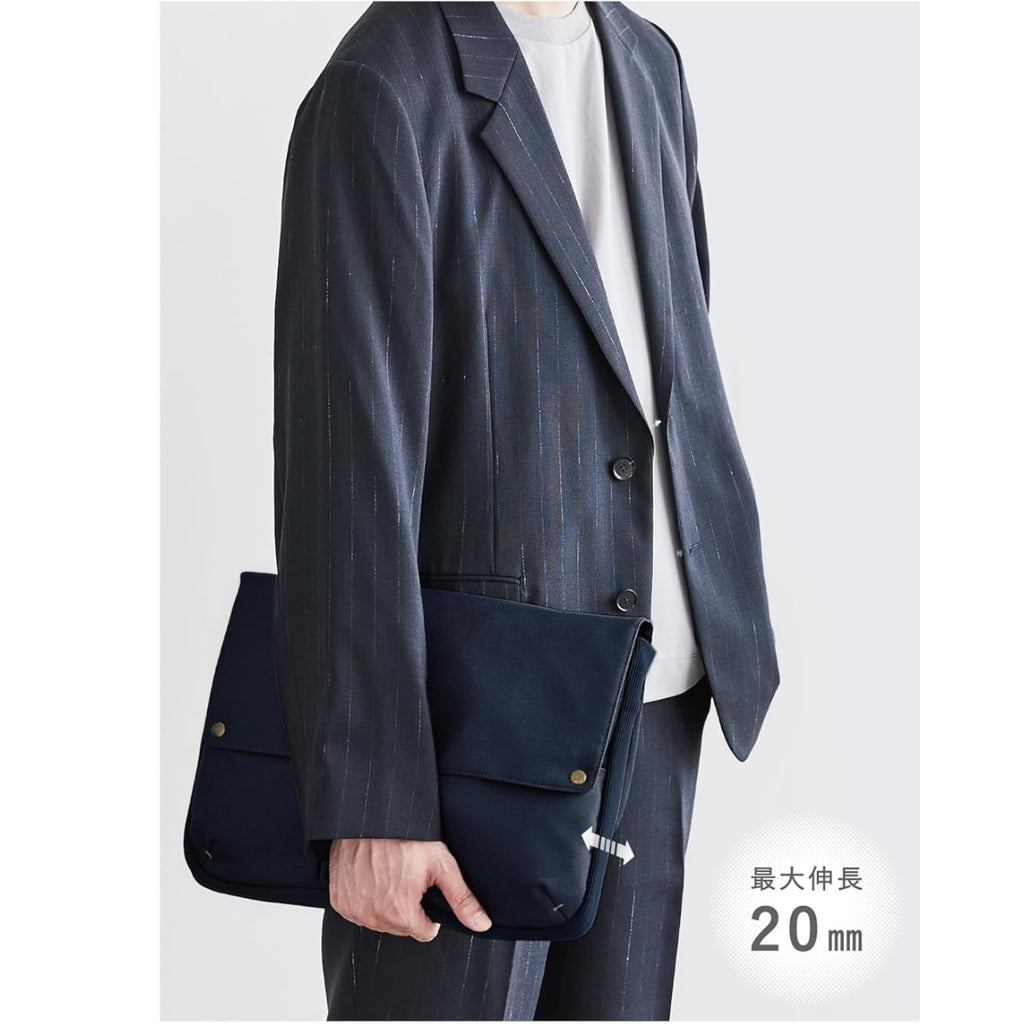 Navy Kokuyo Bizrack Bag-in-Bag held under the arm of a person wearing a dark pinstripe suit, showing its slim 20 mm expandable design.