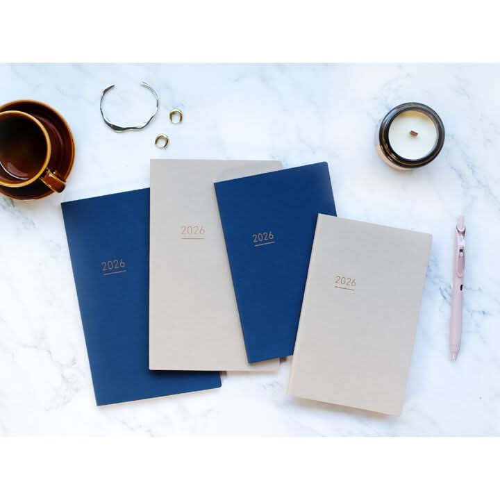 Flatlay of Kokuyo Jibun Techo Lite 2026 Mini B6 Slim Diaries in navy and beige with stationery accessories.